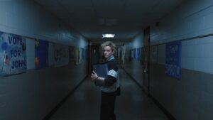 A young female teacher stood alone in a dark school hallway.