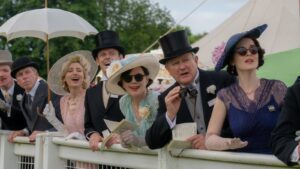 Downton Abbey characters in formal attire enjoying a lively day at the horse races.
