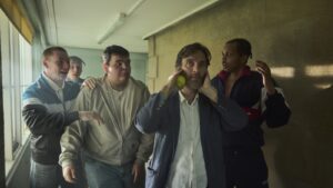 Cillian Murphy as a teacher in a crowded school corridor with rowdy students, holding a tennis ball and covering his ears.
