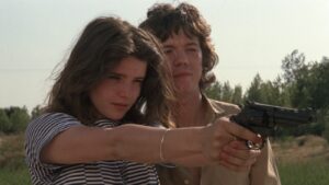 A pair of young people point a gun at an unknown target