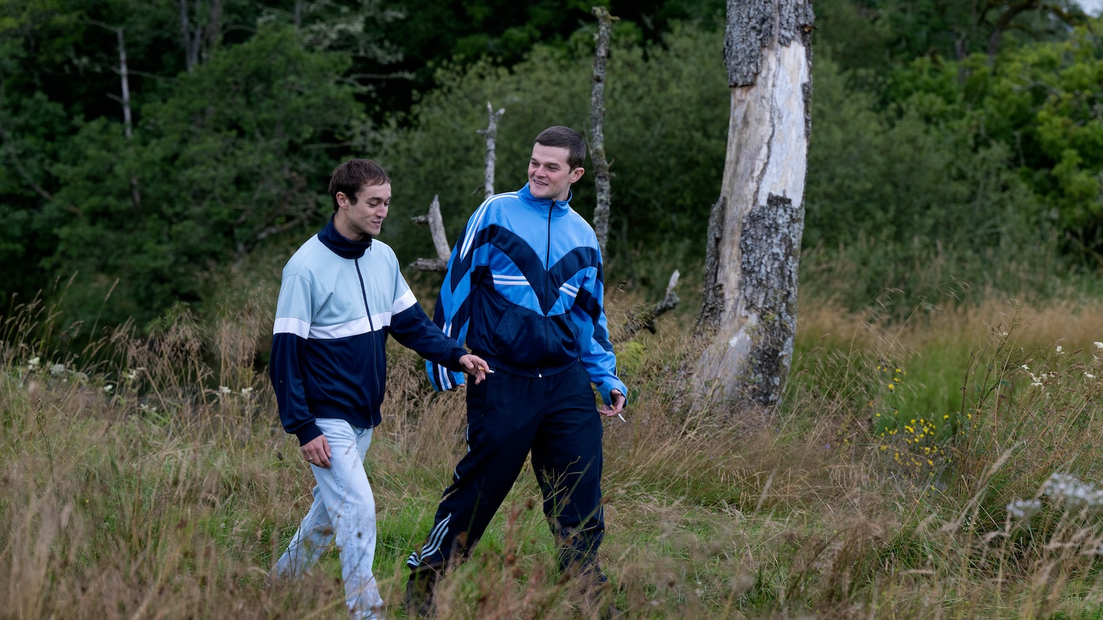 I Swear - Publicity & Production Stills 2024 Two young men in tracksuits walking across a field.