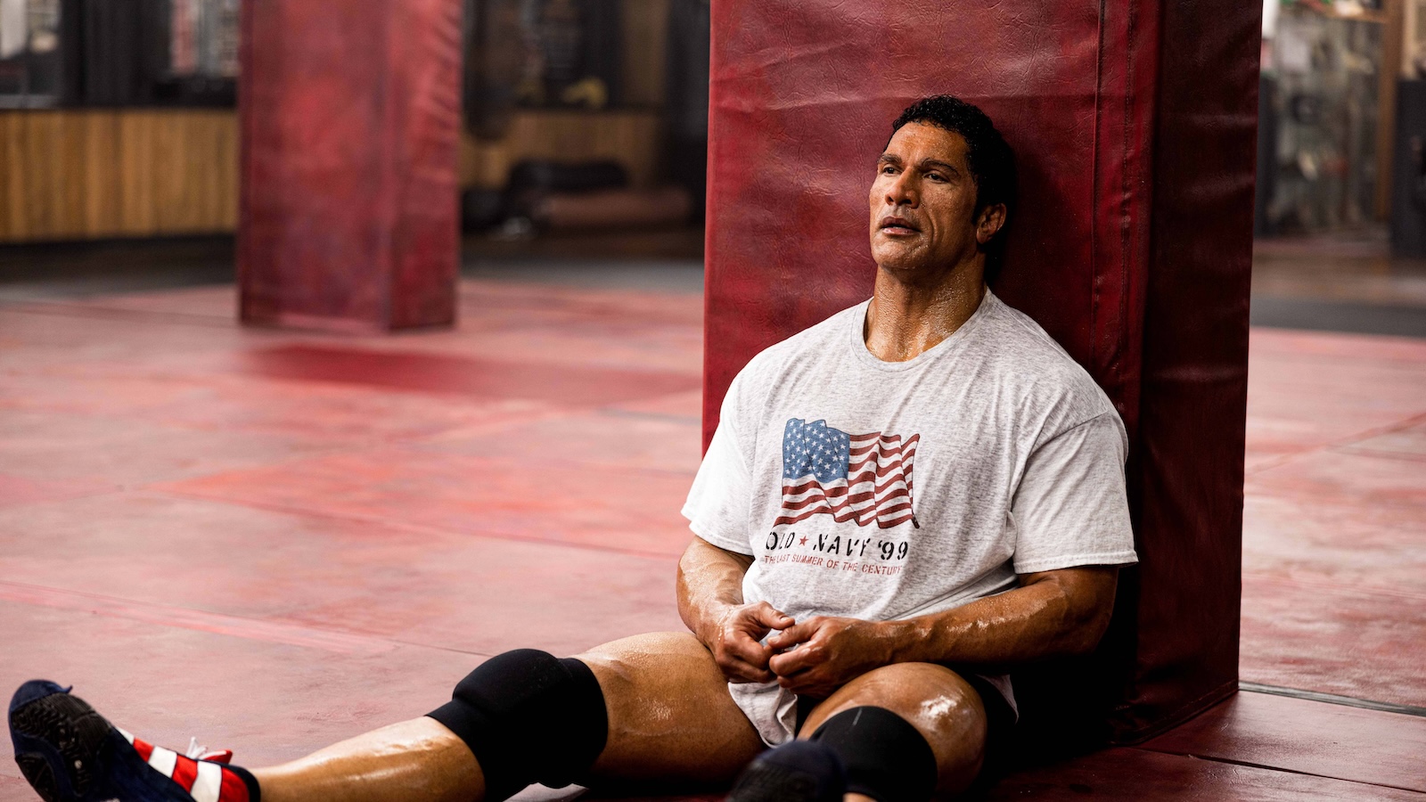 The Smashing Machine A muscular, middle-aged MMA fighter sitting down in an empty gym.