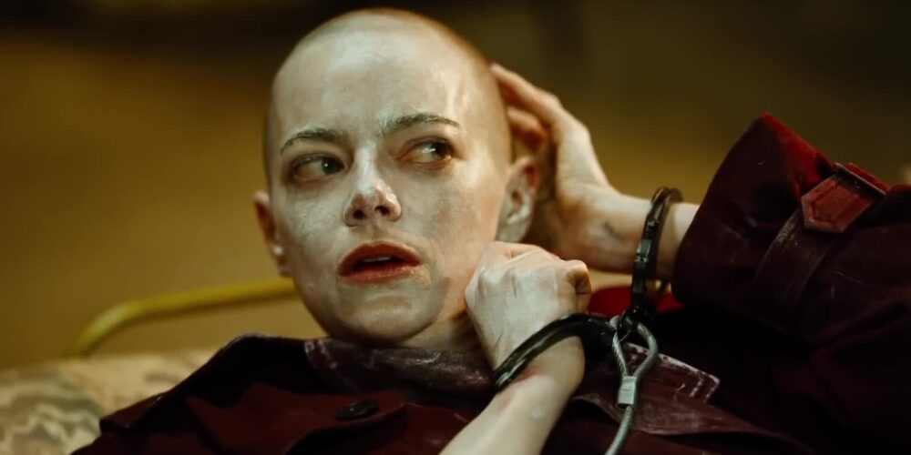 Emma Stone, complete with shaved head, handcuffs and seemingly covered in a white lotion, looks shocked.