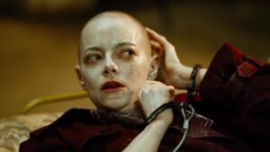 Emma Stone, complete with shaved head, handcuffs and seemingly covered in a white lotion, looks shocked.
