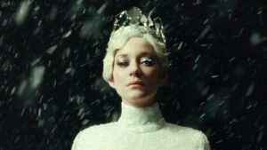 Marion Cotillard looks fierce with a glittery white dress, white hair, silver eye makeup and a glass crown, surrounded by falling snow