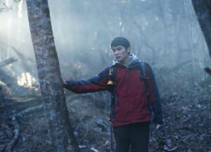 A young Japanese man wanders alone through a wooded area.
