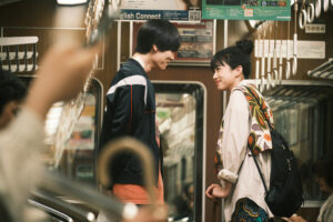 A young Japanese man and woman stood together in a train carriage.